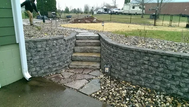 Stacked stone retaining walls with gravel base and landscape lighting along stepped entry