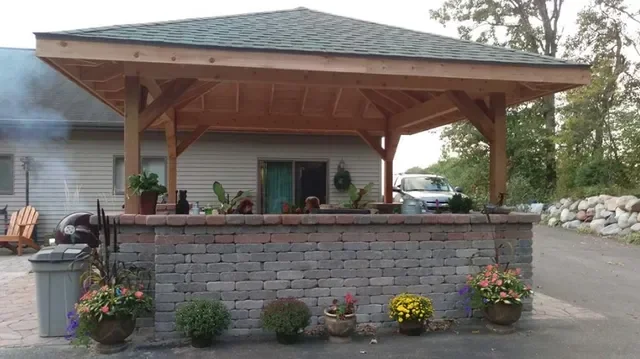 Wooden pergola over gray block retaining wall with planted flower beds and landscaping