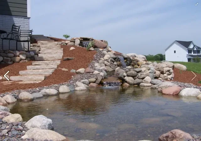 Backyard pond with boulder edging, tiered stone steps, and mulched landscape beds