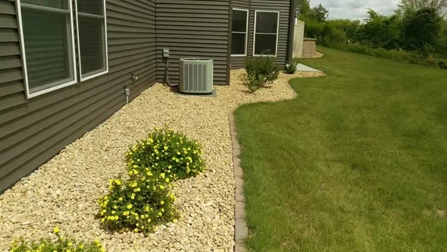 River rock mulch beds with yellow flowering shrubs and brick edging along home foundation