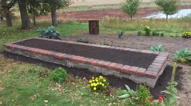 Raised garden bed with concrete block base and red brick border filled with dark mulch and plantings