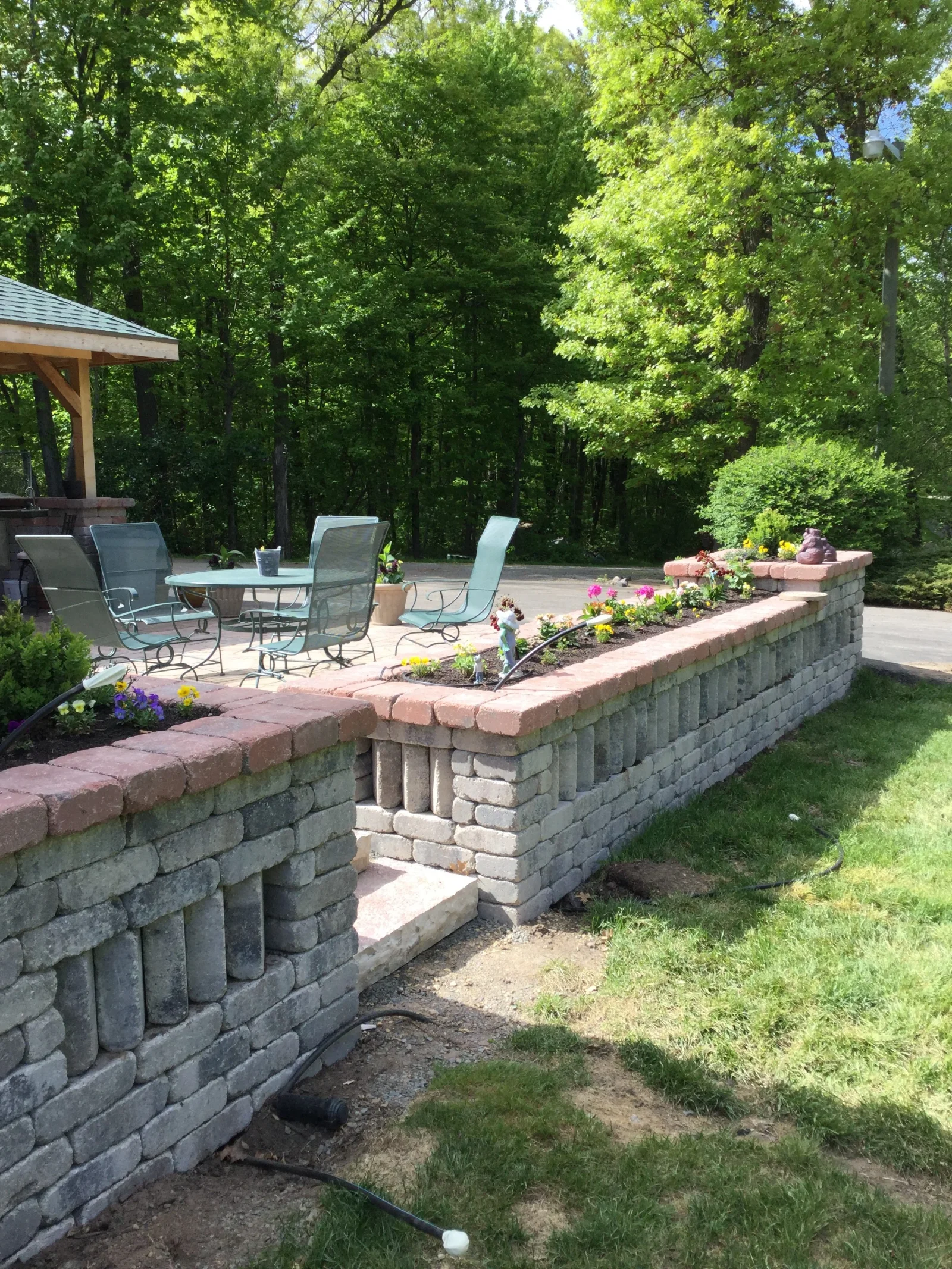 Concrete block retaining wall with brick cap, raised planter beds with colorful flowers and shrubs