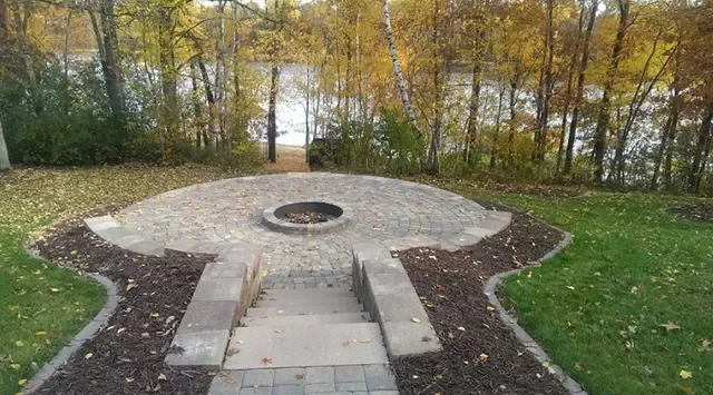 Circular paver patio with central fire pit, concrete seating walls, and mulched landscape beds