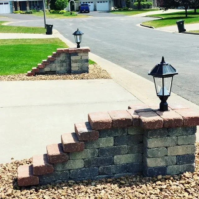 Tiered concrete block retaining wall with landscape lighting and river rock base