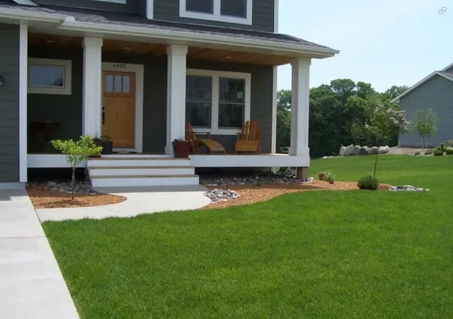 Front lawn with seeded grass, mulched beds, concrete walkway, and ornamental plantings