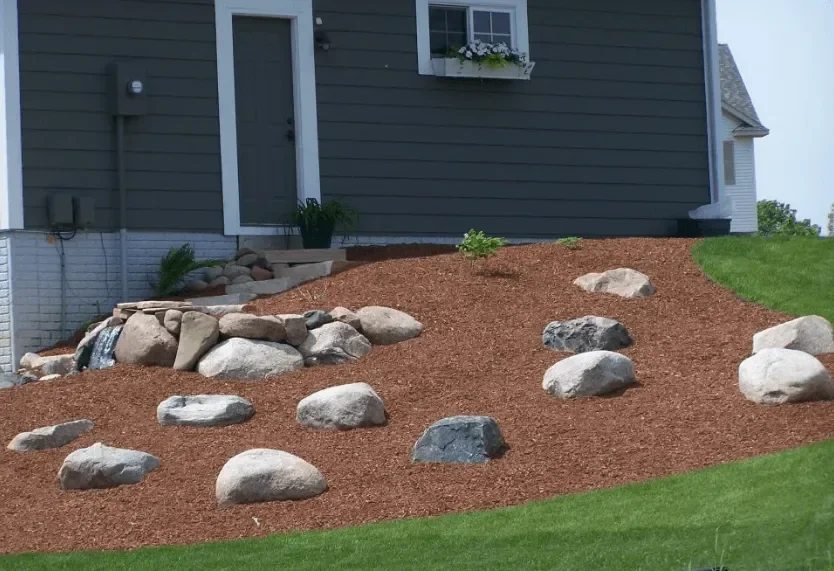 Brown mulch landscape bed with white and gray boulders along home foundation