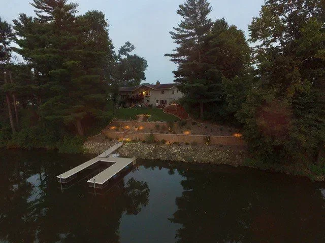 Waterfront landscape with tiered stone retaining walls, gravel beds, and integrated landscape lighting at dusk