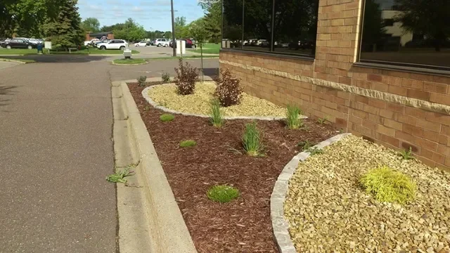 Landscape beds with brown mulch, tan stone, concrete edging, and ornamental plants along brick building