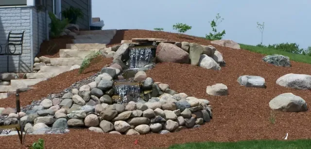 Drainage pipe installation with river rock and mulch erosion control on sloped terrain