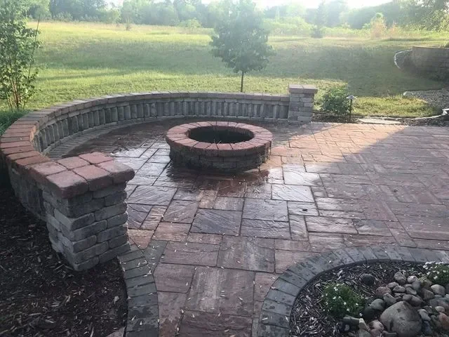 Curved brick patio with central fire pit and curved seating wall in open yard setting