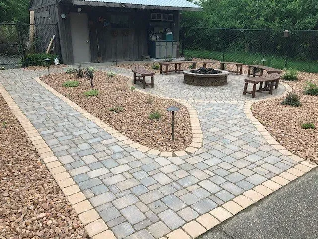 Paver patio with fire pit, benches, and gravel landscaping near modern building