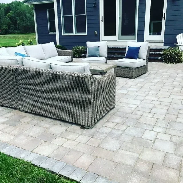 Gray paver patio with woven wicker sectional seating and potted plants against modern home