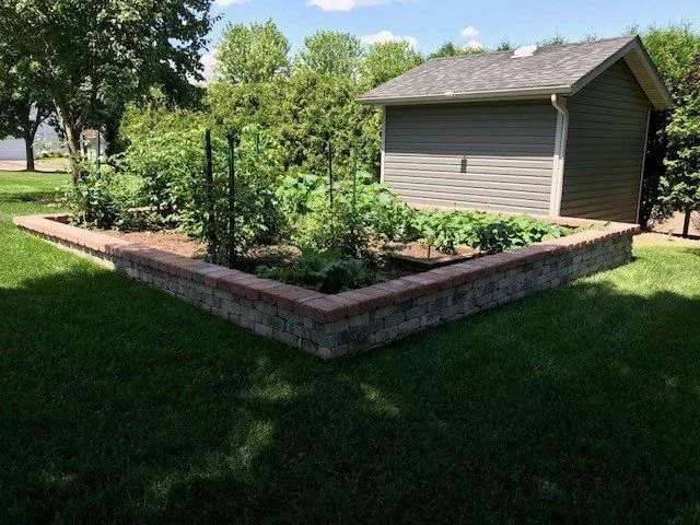 Brick raised garden bed with mulch, vegetables, and wooden trellis structures