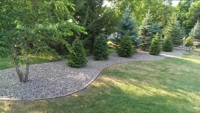 River rock mulch bed with evergreen shrubs and curved edging against lawn