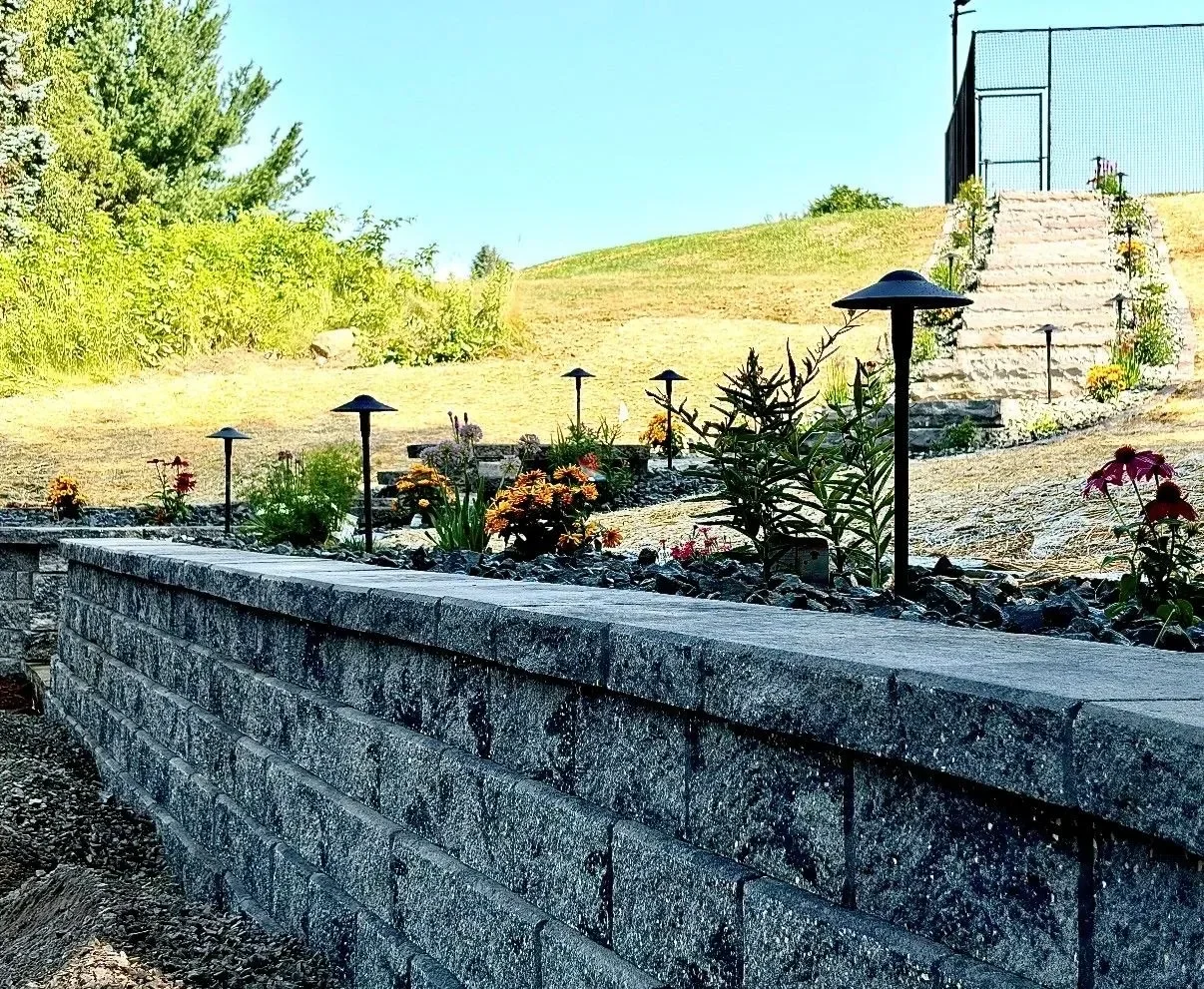 Stone retaining wall with landscape lighting and flowering perennial beds on hillside